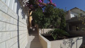 A narrow pathway leading to a building with a stone wall on one side and a planter with plants on the other. - Apartments Maritimo - Comfort Two Bedroom Apartment with Sea View and Terrace (Smokvica)