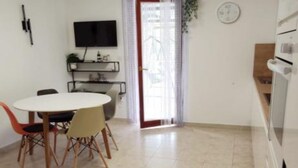 A compact living space with a dining area, a flat-screen TV mounted on the wall, a sliding glass door leading to a balcony, and a kitchenette with a microwave and oven. - Apartments Maritimo - Comfort Two Bedroom Apartment with Sea View and Terrace (Smokvica)