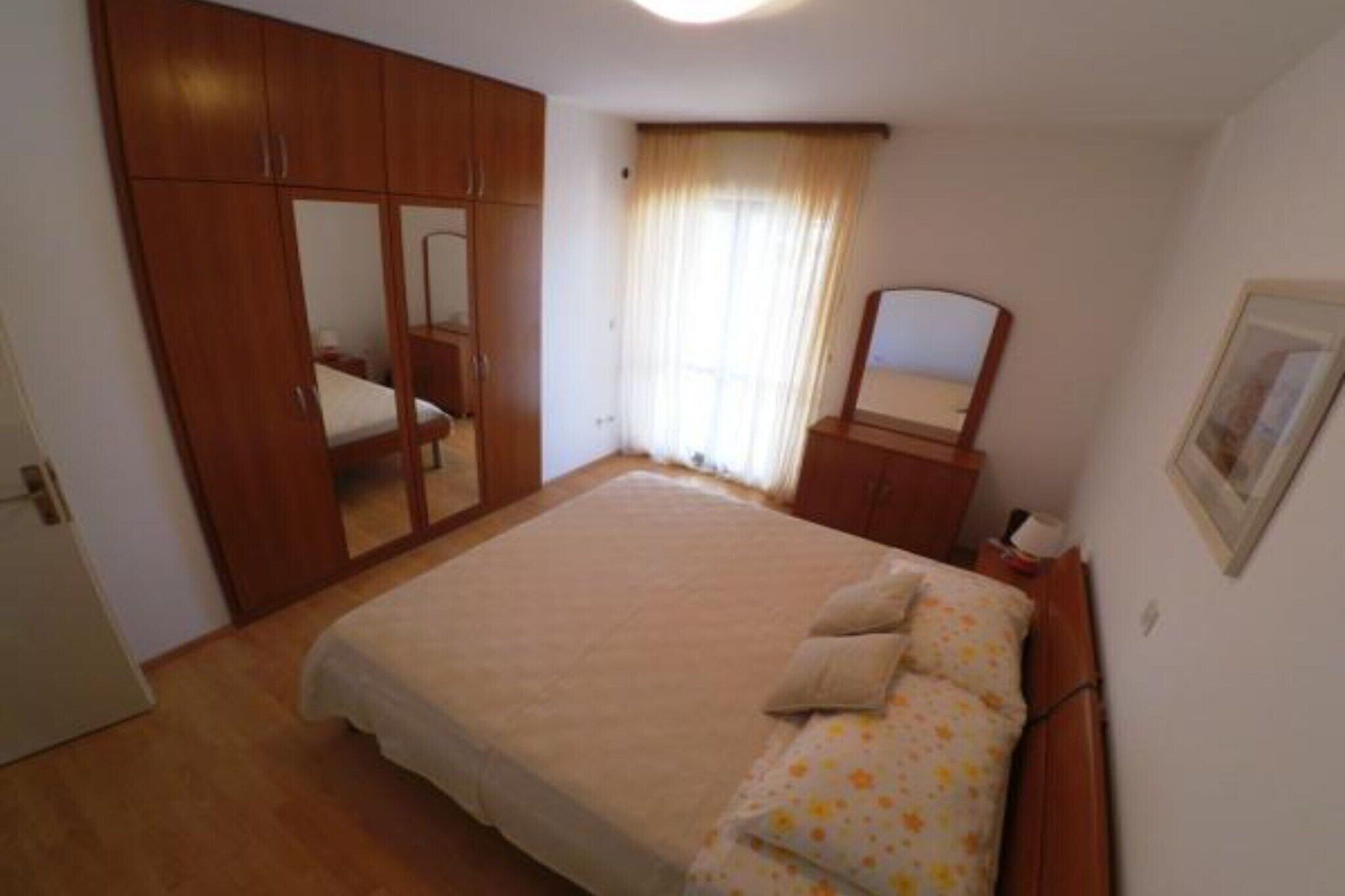 Un dormitorio con cama, armario, espejo y ventana con cortinas.