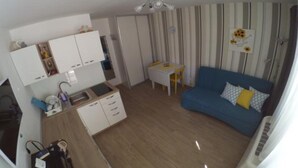 A compact living space with a kitchenette, a dining area, and a blue sofa with a yellow pillow.