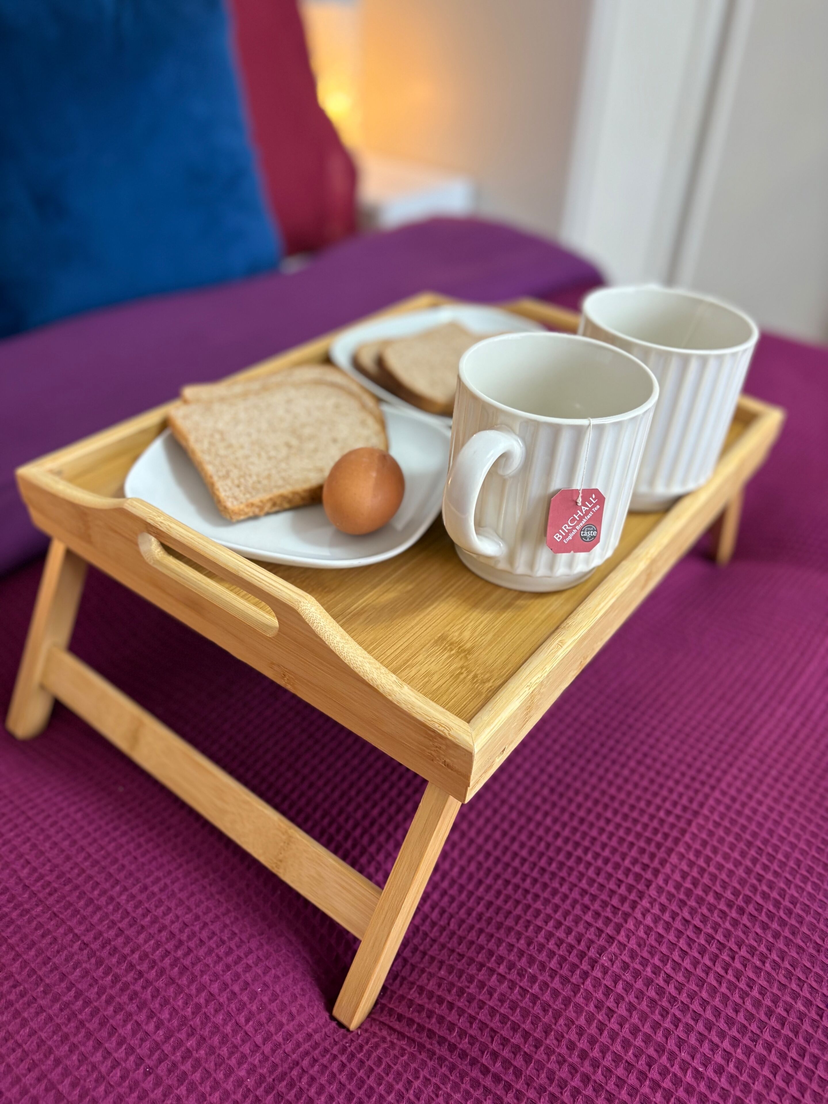 A wooden tray with a white mug and two plates of toast and an egg on a purple textured surface.