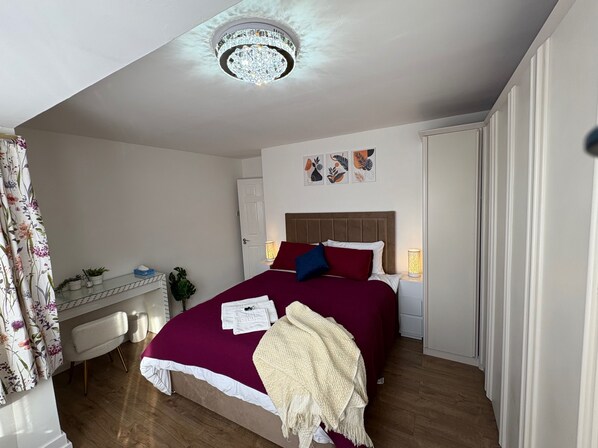 A bedroom with a large bed, a desk with a chair, a ceiling light fixture, and a door.