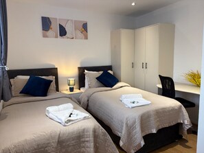 Une chambre d’hôtel avec deux lits, un bureau, une chaise et une armoire.