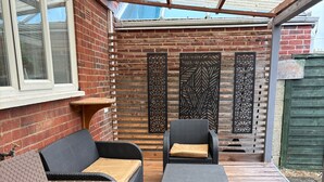 Un patio couvert aménagé avec des meubles en osier, un mur en briques et des panneaux décoratifs.