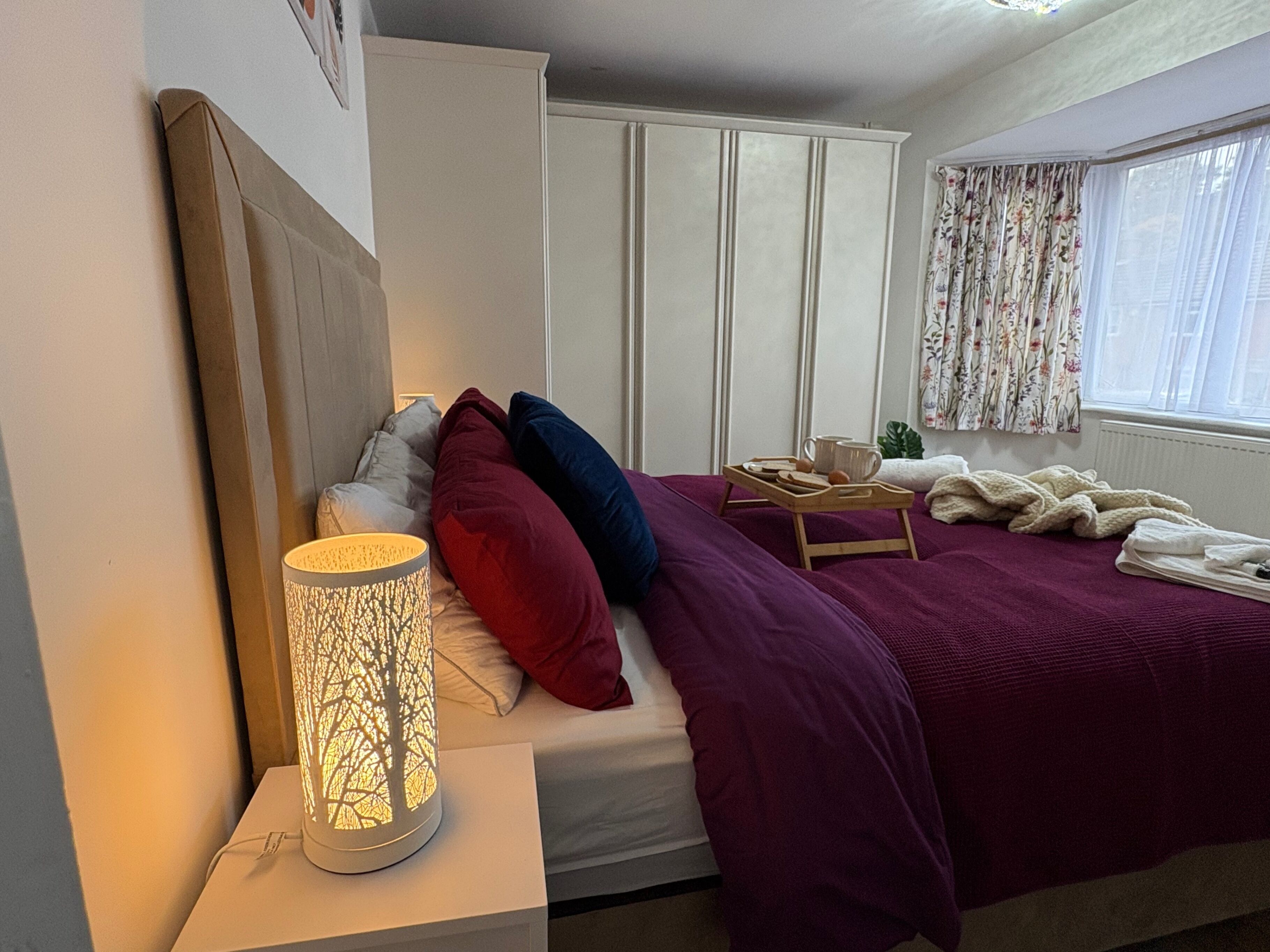 A bedroom with a bed, a bedside table with a lamp, a wardrobe, and a window with curtains.