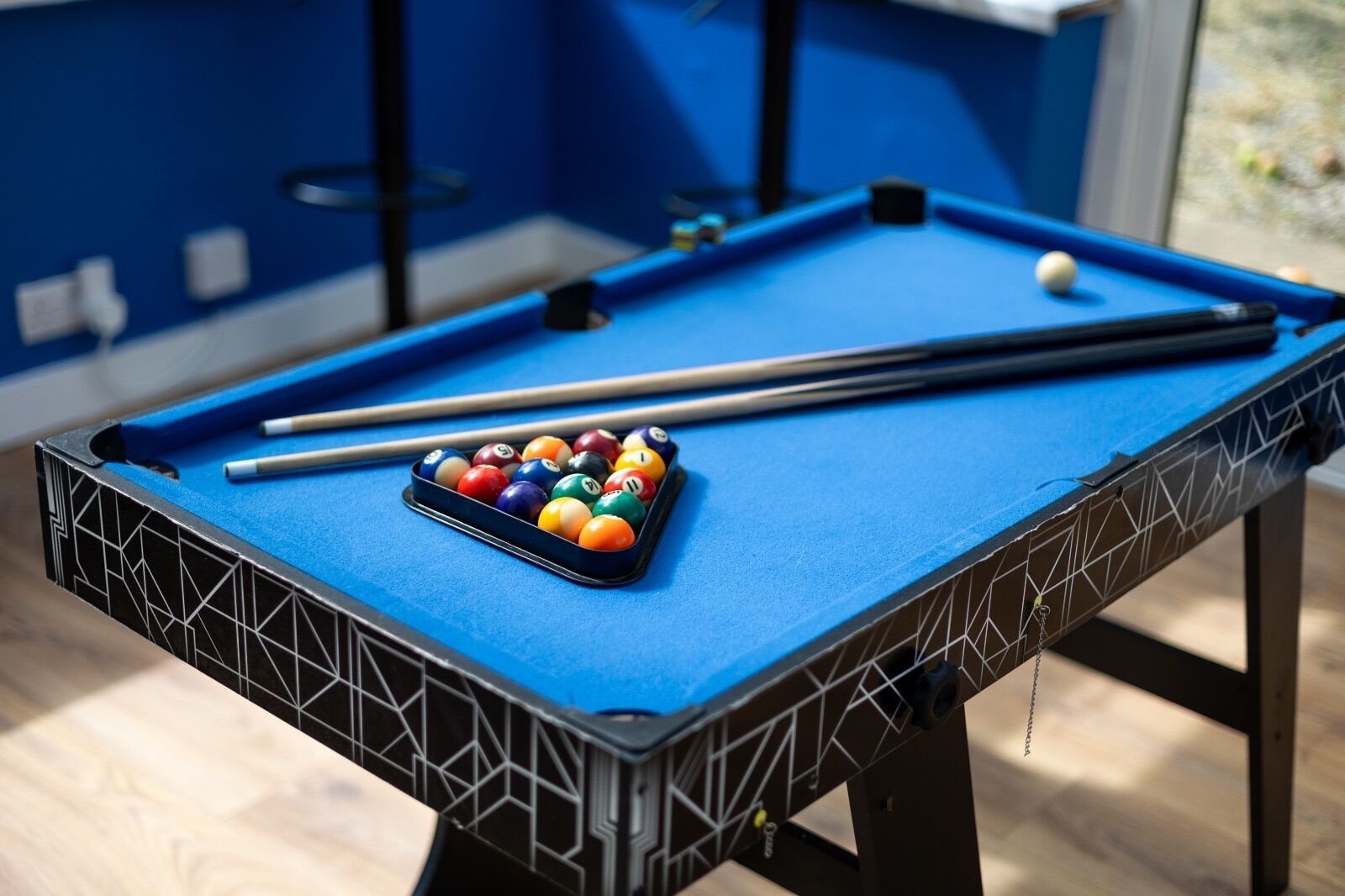 A pool table with a blue felt surface, a set of pool cues, and a rack of billiard balls.