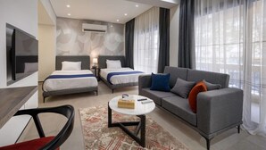 A modern hotel room with two beds, a sofa, a TV, and a large window with curtains.