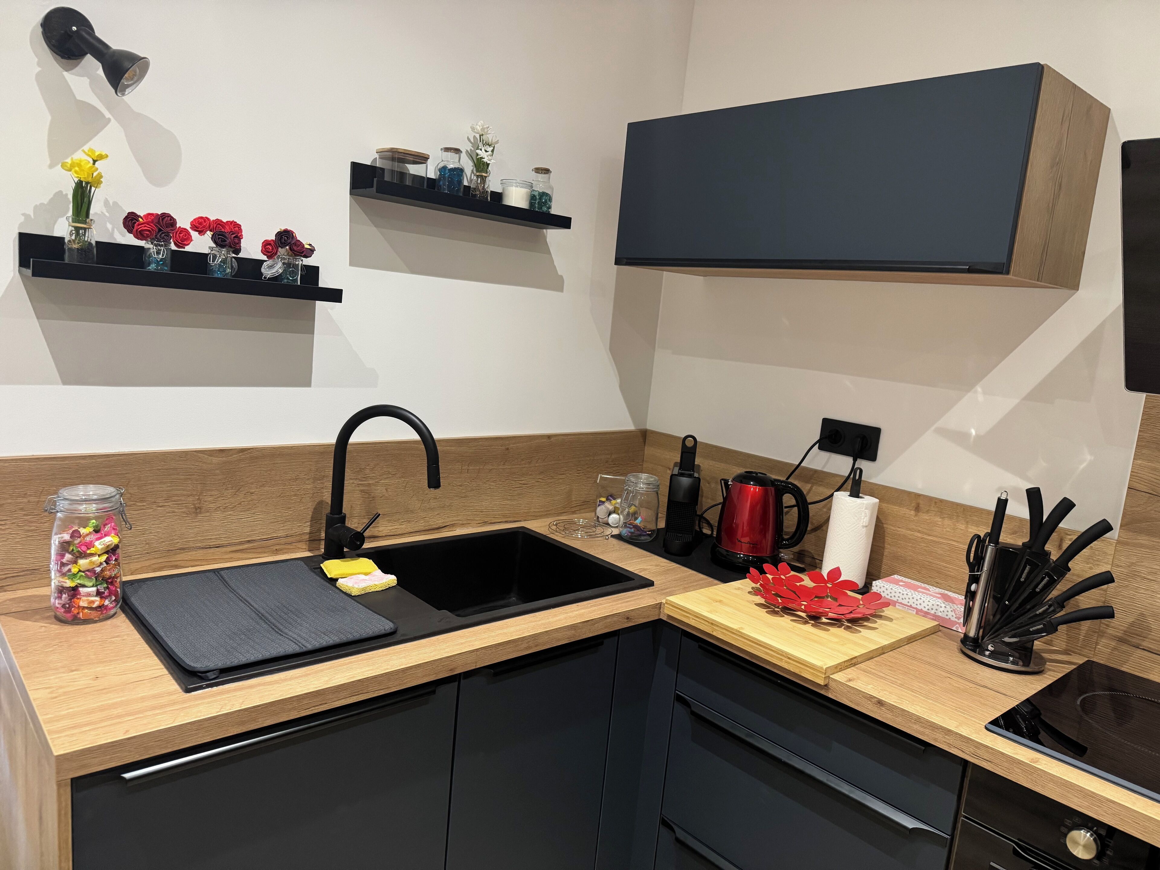 Une cuisine moderne avec un évier noir, des plans de travail en bois, un four encastré et un meuble noir au-dessus du plan de travail.