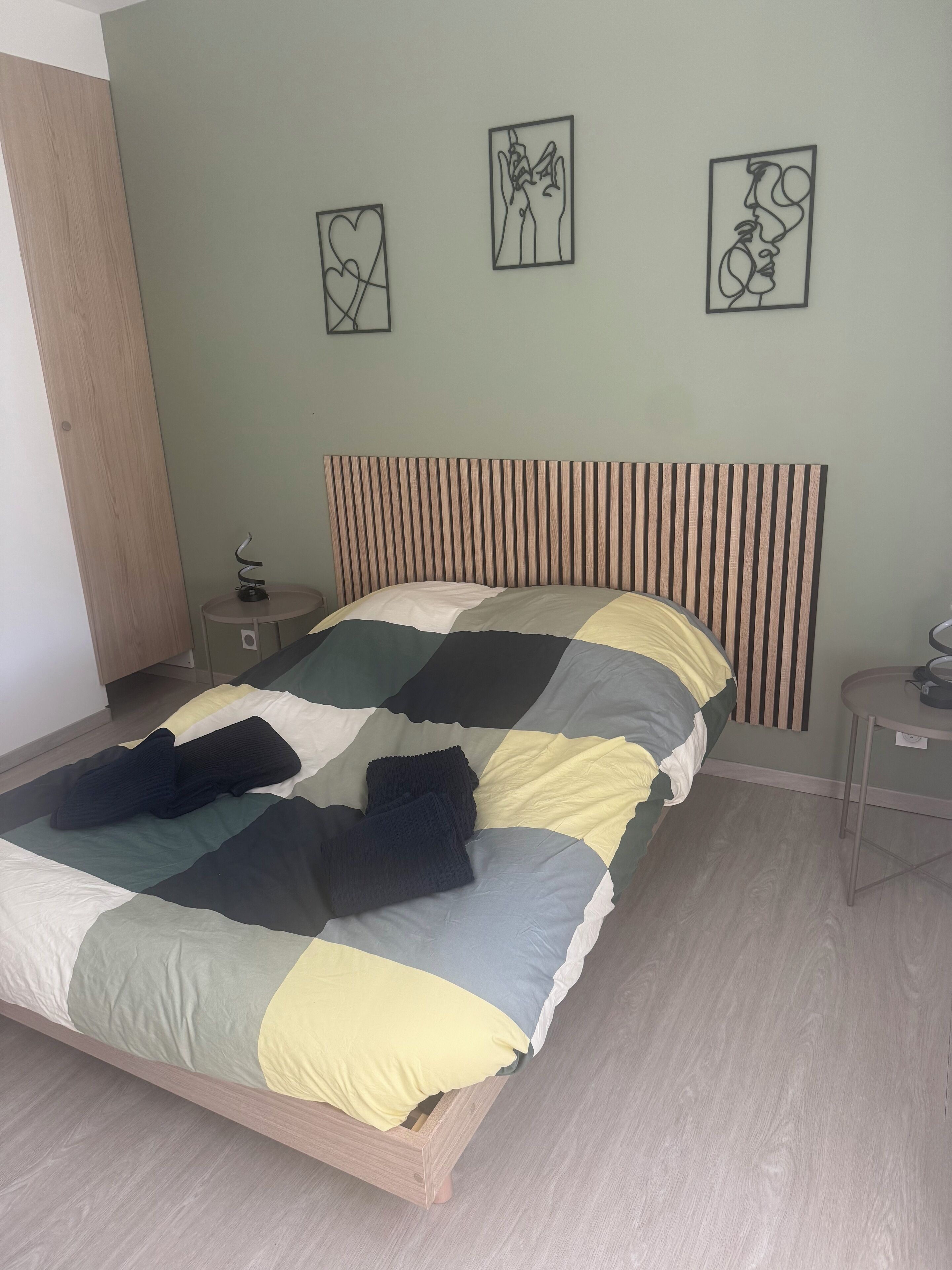 A bedroom with a bed, a nightstand, a wooden headboard, and three wall art pieces.