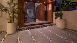 Un edificio moderno con estructura de varios pisos, una entrada acogedora con puertas de madera y plantas en macetas al nivel del suelo.