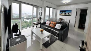A modern living room with a large window, a white table, a black sofa, and a ceiling fan. - Breeze Residences Condos (Pasay)