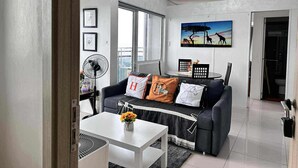 A modern living room with a grey sofa, a white coffee table, and a painting of giraffes. - Breeze Residences Condos (Pasay)