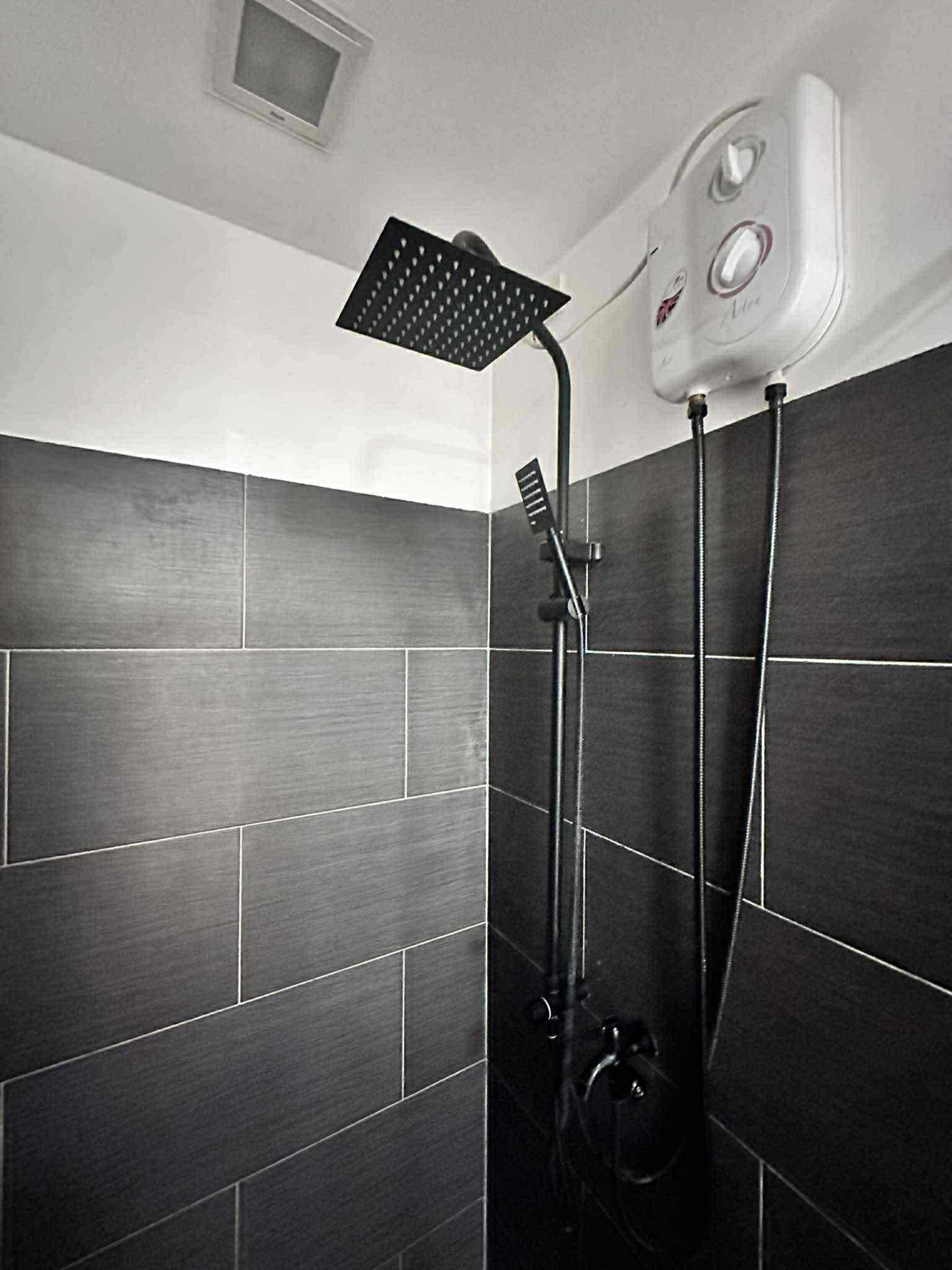 A modern bathroom with dark tiled walls, a shower with a square showerhead, and a control panel.