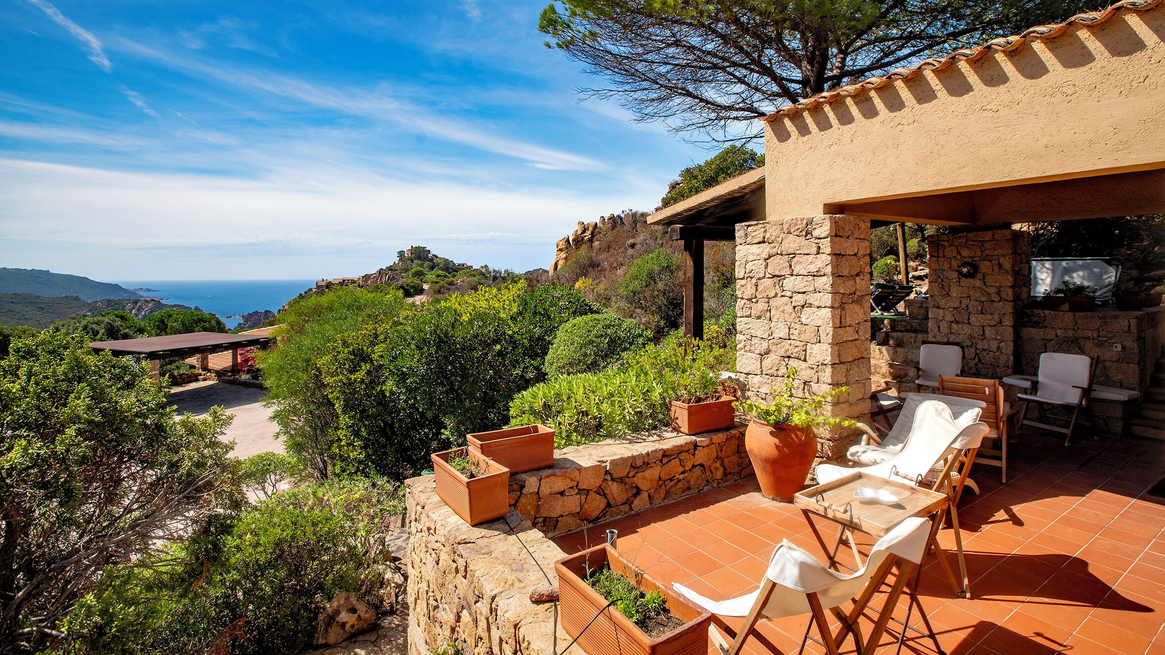 A patio with outdoor furniture, a stone wall, and a view of the sea.