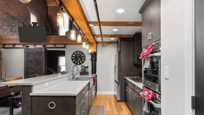 A modern kitchen with a central island, stainless steel appliances, and exposed wooden beams. - Two Story Penthouse - Walk to the Convention Ctr (Indianapolis)