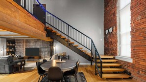 A spacious loft with a wooden staircase, a dining area, and a cozy seating space. - Two Story Penthouse - Walk to the Convention Ctr (Indianapolis)