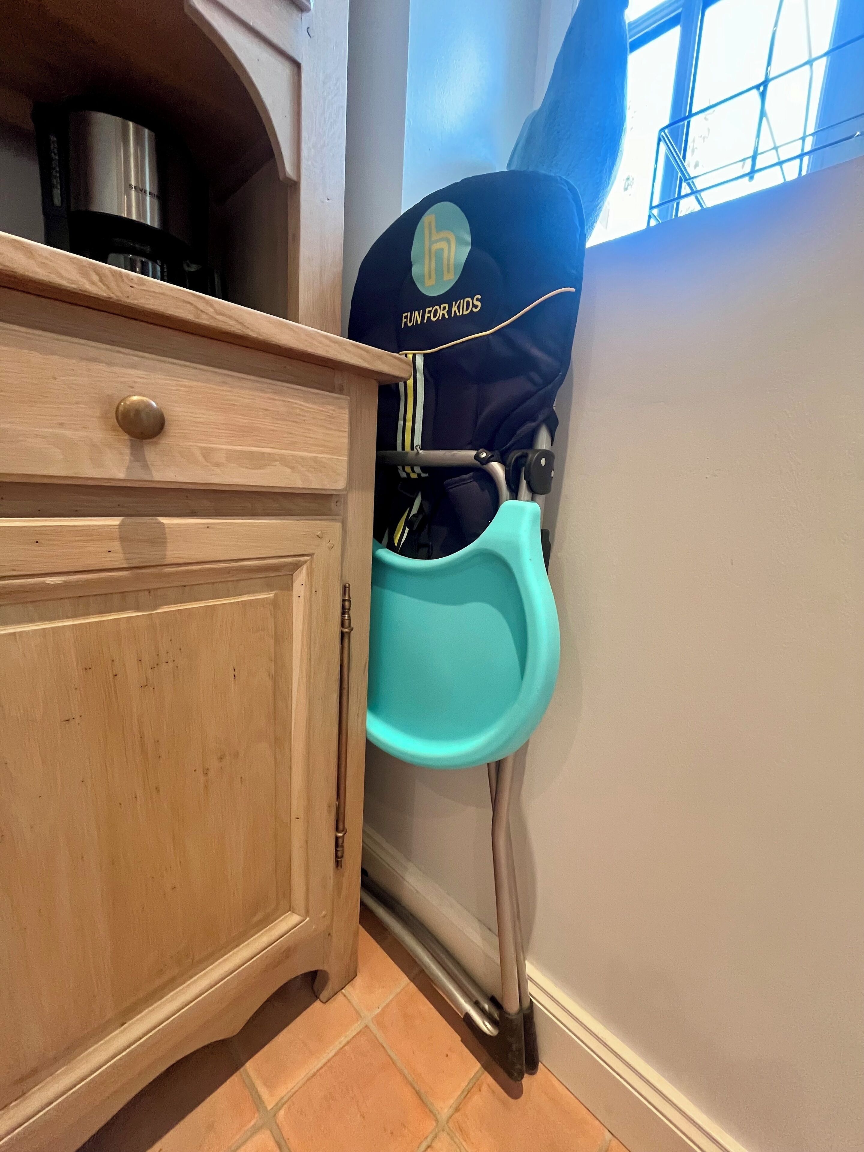 A kitchen with a wooden cabinet, a teal baby stroller, and a window with a metal railing.