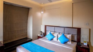 A hotel room with a large bed, a ceiling fan, a nightstand, and a window with curtains. - The Sky Court - An Hospitality (Chhatrapati Sambhajinagar)