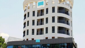 A multi-story hotel with a curved facade, balconies on each floor, and a prominent logo on the top. - The Sky Court - An Hospitality (Chhatrapati Sambhajinagar)
