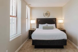 A bedroom with a large bed, two bedside tables, a wall-mounted mirror, and two floor lamps.
