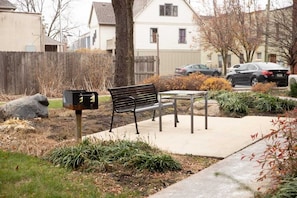A bench and mailbox in a residential area with houses in the background.