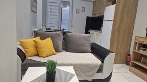 A compact living space with a sofa, a small table with a plant, and a kitchenette in the background. - N&S Fms, Cozy two bedroom apartment close to Fleming Metro station (Thessaloniki)