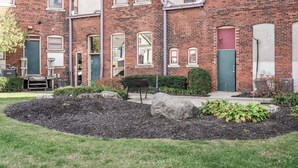 Un bâtiment en briques doté de nombreuses fenêtres et portes, d’un banc et d’un espace jardin aménagé.