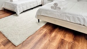 Un dormitorio con dos camas, un tapete blanco y suelo de madera.