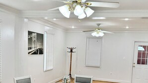 Comedor con una mesa redonda, sillas blancas, ventilador de techo y un cuadro en la pared.