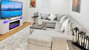 Una sala de estar moderna con un televisor de pantalla plana, sofá gris, mesa de centro de madera y ventilador de techo.