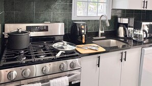 Una cocina moderna con armarios blancos, estufa a gas, cafetera y ventana con vista a zonas verdes.