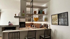 Una cocina con isla central, taburetes de bar y estantes con objetos decorativos.