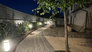 Un sendero pavimentado con farolas, un árbol y un edificio al fondo.