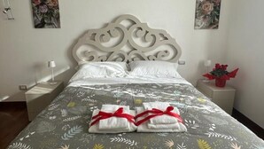 Una cama bien tendida con ropa de cama estampada con motivos florales y dos toallas adornadas con lazos rojos.