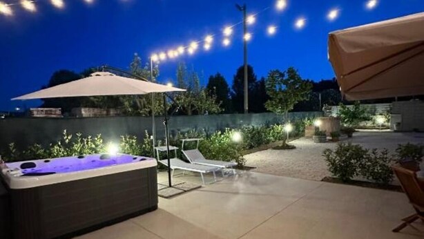 Un patio exterior con un jacuzzi, sillones de descanso y luces colgantes.