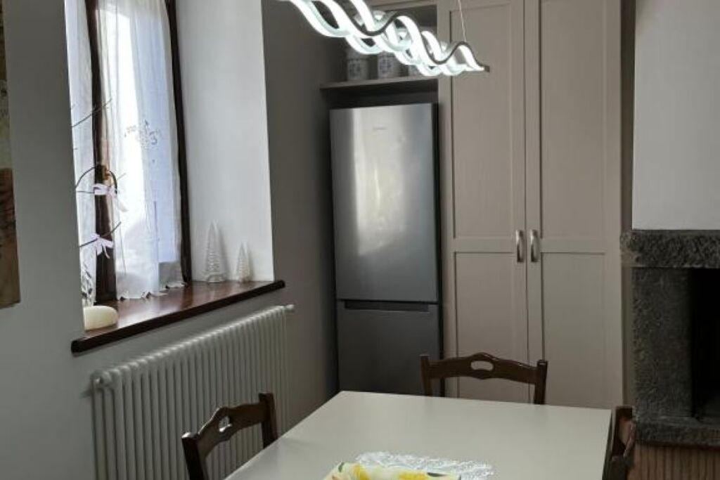 A dining area with a table, chairs, a refrigerator, and a window with curtains.