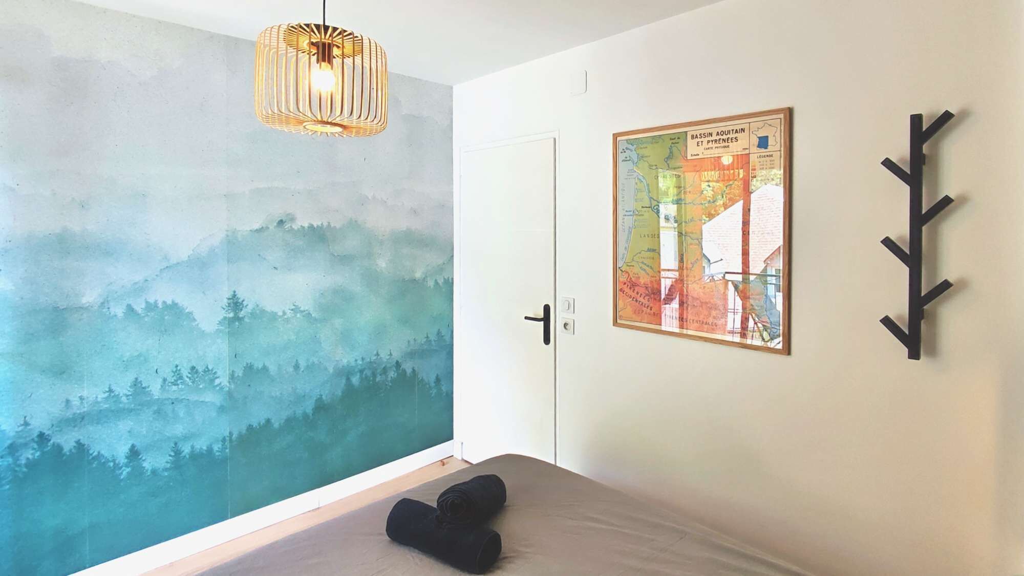 A bedroom with a mural, a bed, a hanging light, a door, and a map on the wall.