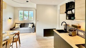 A modern kitchen with a built-in island, a dining area with a wooden table and chairs, and a cozy seating area with a sofa and cushions. - New apartment for 6 people - close to the city center (Bagnères de Luchon)
