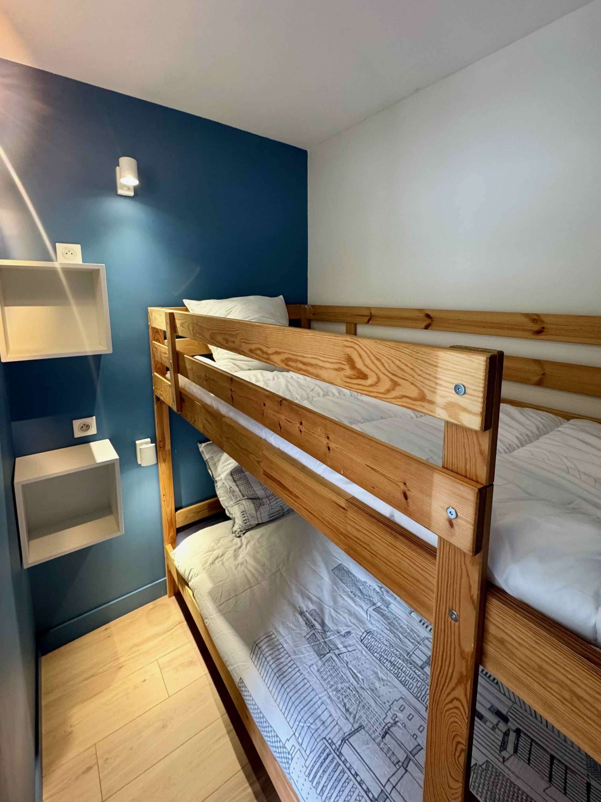 Een stapelbed in een kamer met een blauwe muur, een witte plank en een houten vloer.