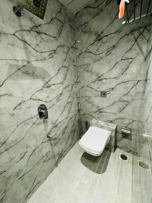A bathroom with a marble wall, a toilet, a shower, and a towel rack. - Hotel Bellamont (Mumbai)