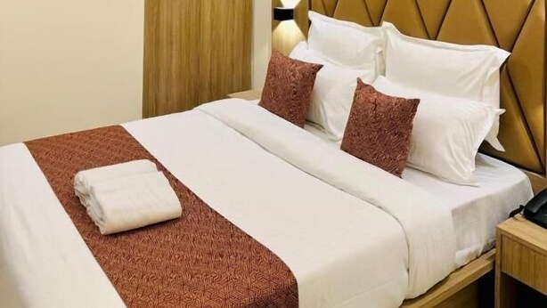 Una habitación de hotel con una cama, un ventilador de techo, un armario de madera y una lámpara fijada a la pared.