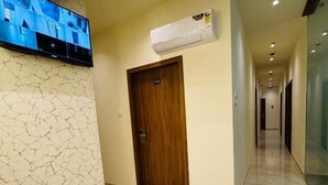 Un pasillo de hotel con piso de mármol, una puerta de madera y un televisor montado que muestra imágenes.