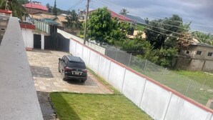 A residential area with a paved driveway, a black car parked, and a well-maintained lawn. - Enyo Home (Tema)