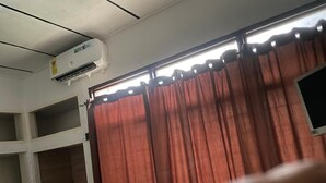 A room with a window covered by a curtain, an air conditioning unit mounted on the wall, and a partially visible door. - Enyo Home (Tema)