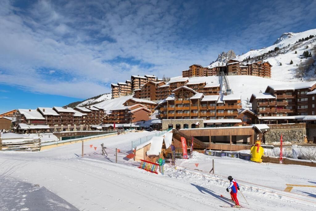 A ski resort with multiple wooden buildings, ski slopes, and a person skiing.