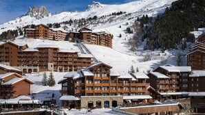 A ski resort with multiple wooden lodges, a ski lift, and a mountainous backdrop.