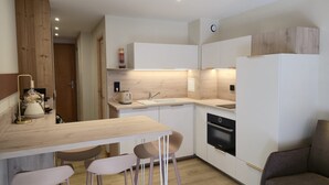 A compact kitchen with a wooden table, bar stools, a built-in oven, and a sink.