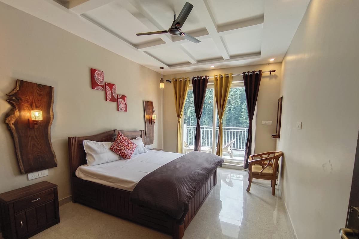 A bedroom with a large bed, a ceiling fan, a wooden headboard, a nightstand, a dresser, a balcony with curtains, and a view of trees.
