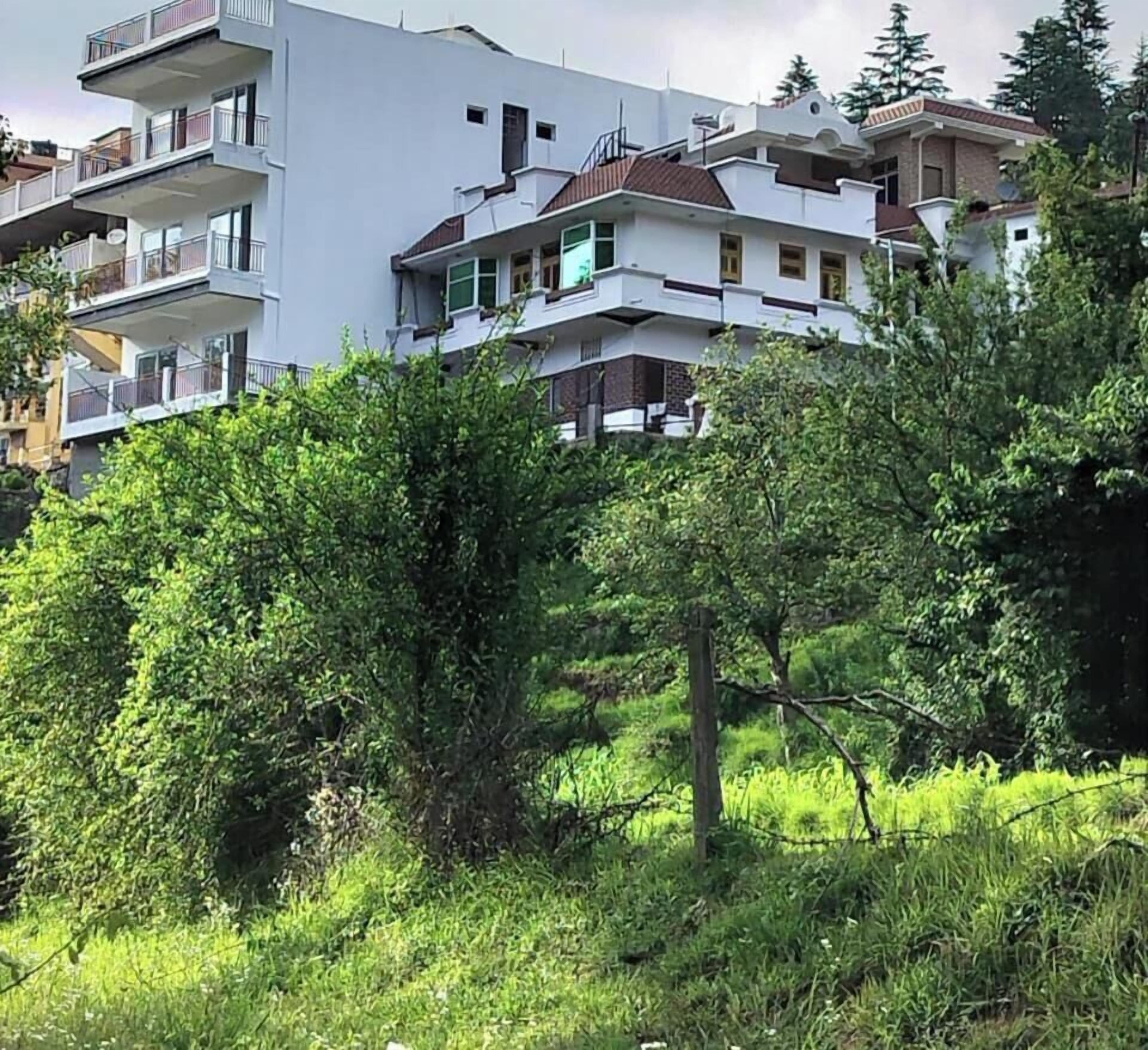 A modern multi-story building with balconies, surrounded by greenery.