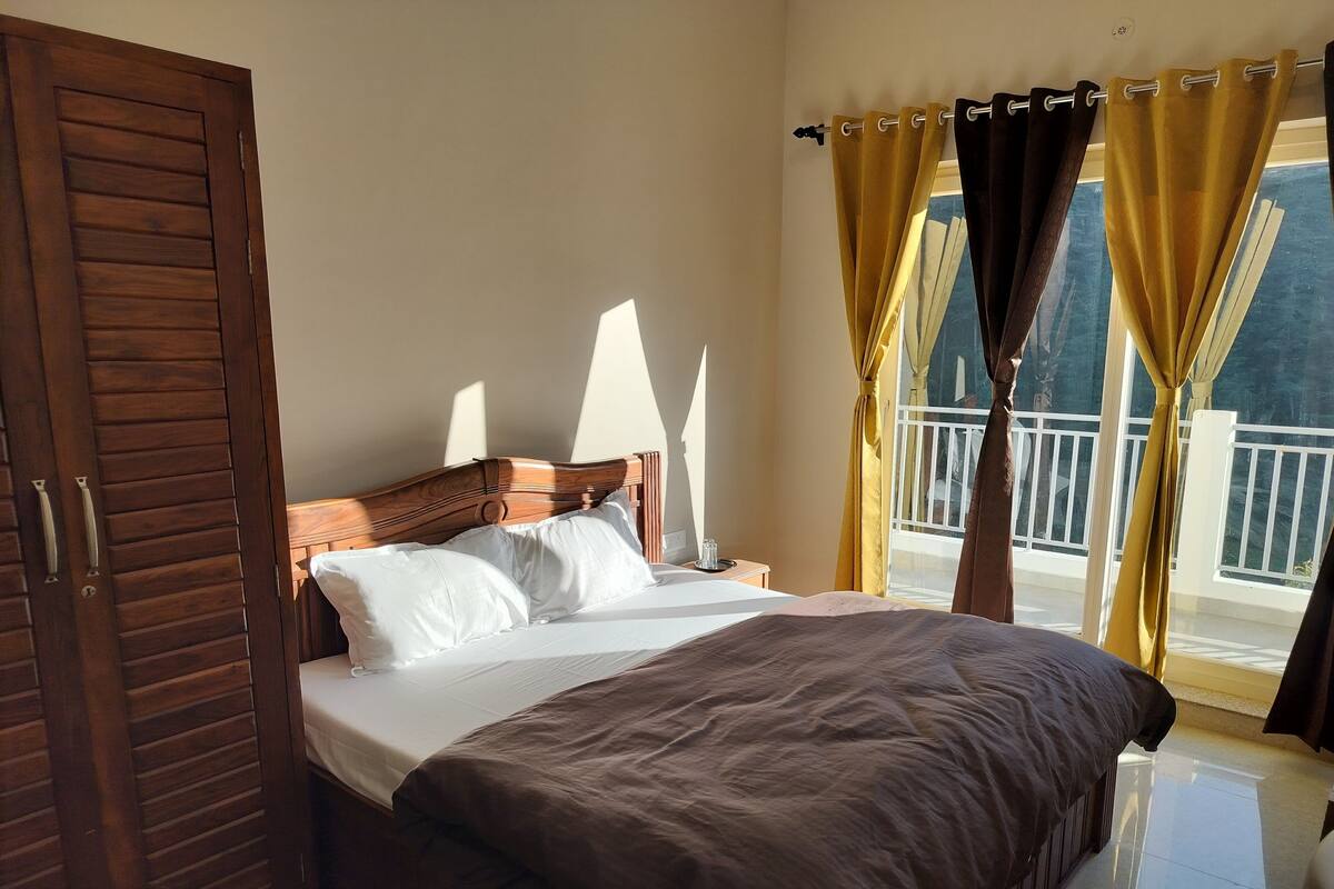 A bedroom with a wooden bed, white pillows, a brown bedspread, and a window with curtains.